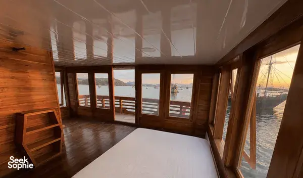 Sunset-lit wooden phinisi shared-cruise cabin with ocean views, hosted by La Famille on a 3D2N Komodo trip in Labuan Bajo