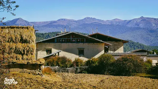 Tibetan lodge building at Ferme Liotard in Shangri-La, set on a hillside above farmland with distant mountain ridges