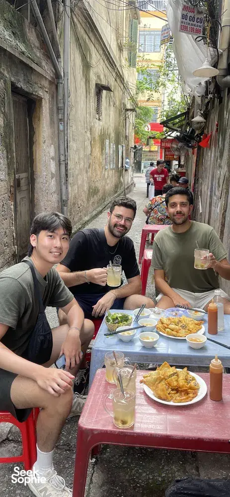 Travellers eating together at a roadside table in a narrow Hanoi lane, part of a beyond-Old-Quarter food adventure