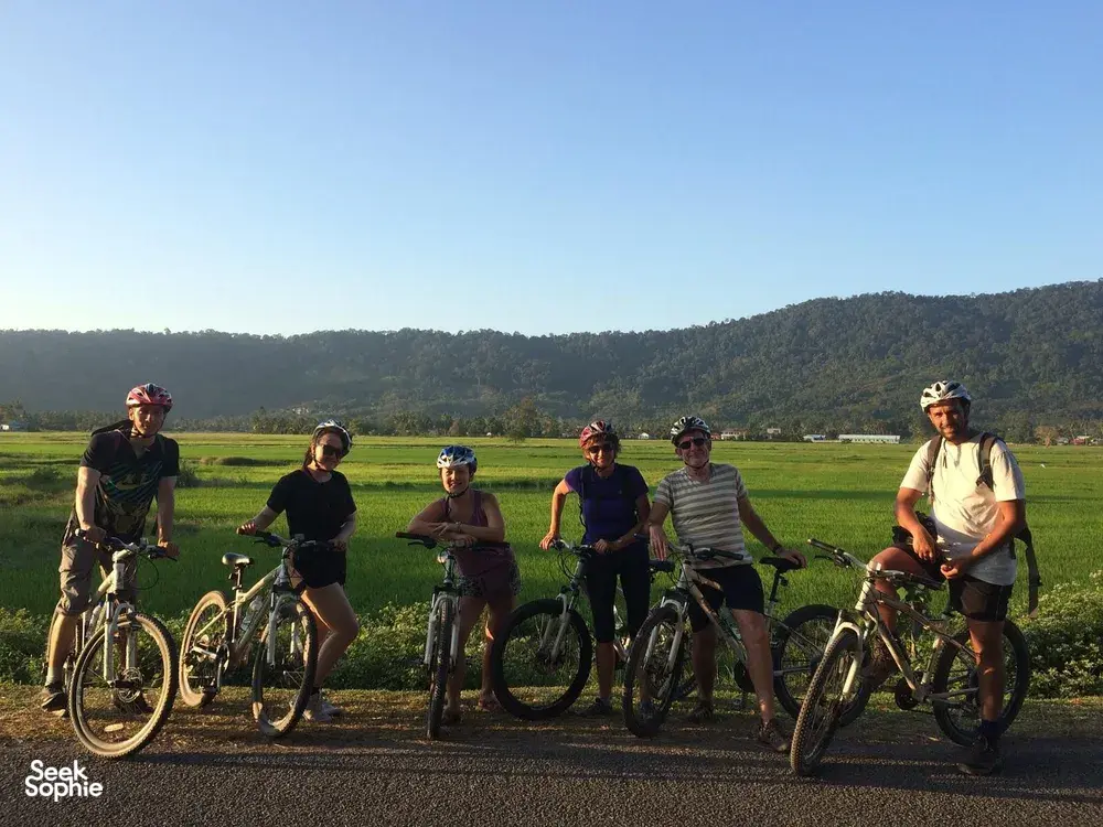 Cyclists with helmets and bicycles paused on a country road through fields and hills in Langkawi on a guided tour