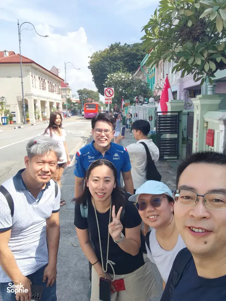 Friends posing on a sunny street with a red kiosk during a real-life Monopoly team game in Katong-Joo Chiat, Singapore hidden gems