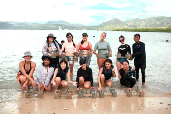 Travellers kneeling at the shoreline, holding cement coral blocks for coral restoration with Rinca Coral Nursery Program in Labuan Bajo