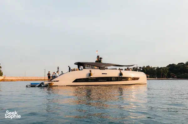Italian luxury yacht in Singapore moving through calm water at dusk, with people relaxing on deck and warm reflections