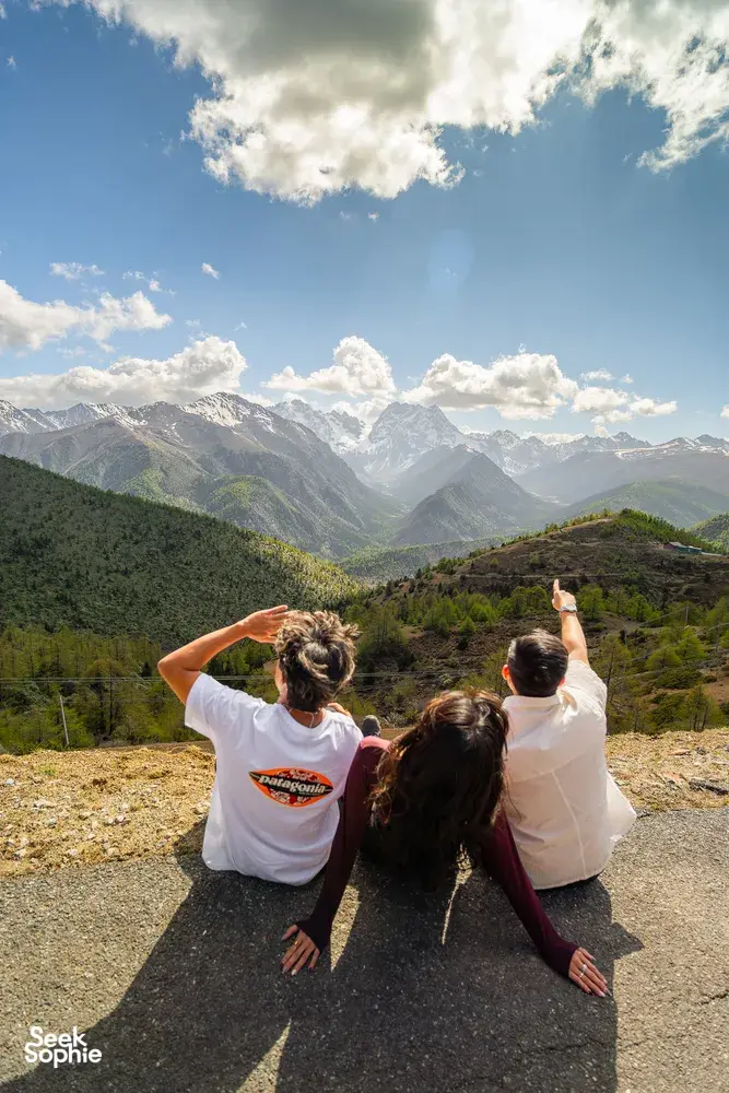 Travellers with arms raised at a high mountain overlook over the Shangri-La valley during a 6-day loop trek