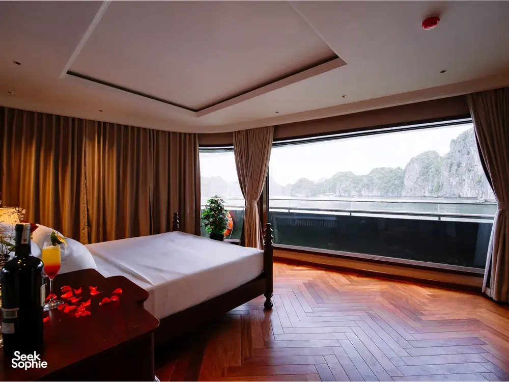 Sunshine Golden Cruises luxe Cat Ba cruise cabin bedroom with a king bed and floor-to-ceiling window over limestone cliffs