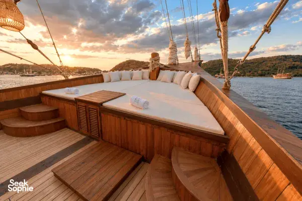 Sunset on a phinisi deck with cushioned lounge benches, railing steps and harbour views across the water in Labuan Bajo