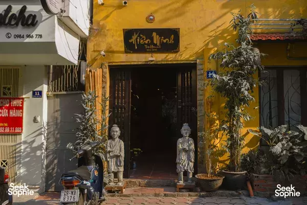 Hien Minh Tea entrance in Hanoi for a zen tea ceremony, framed by stone Buddha statues and leafy potted plants