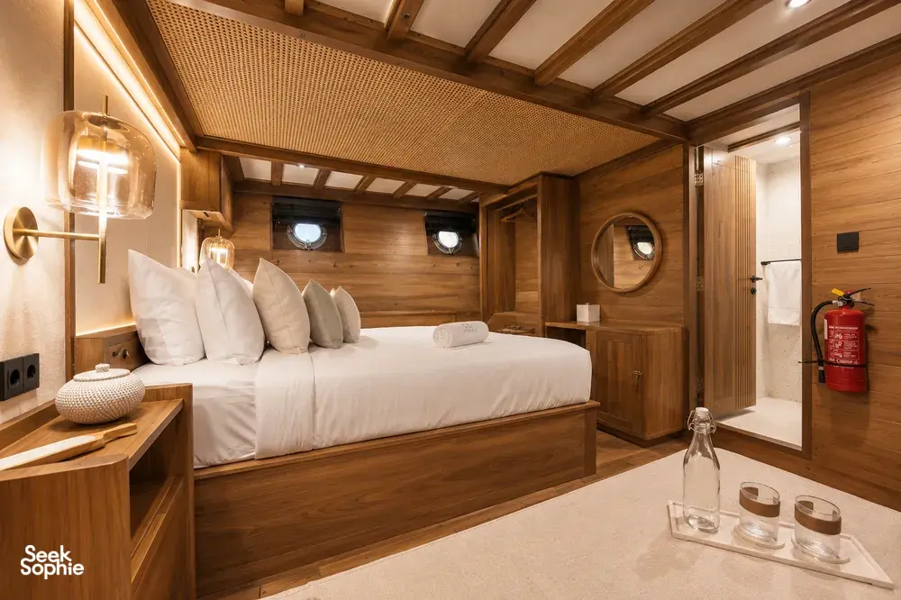Travass Life new phinisi suite with neatly made beds, warm wood finishes, porthole windows and a fire extinguisher for Komodo Island