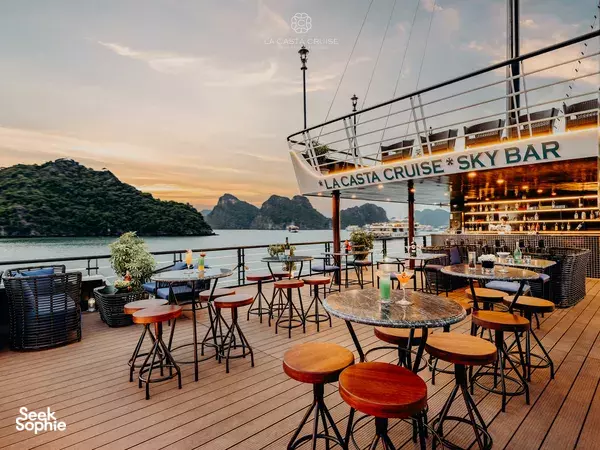 La Casta Cruise sky bar deck with stools and cocktails, glowing at sunset over calm waters in Halong Bay