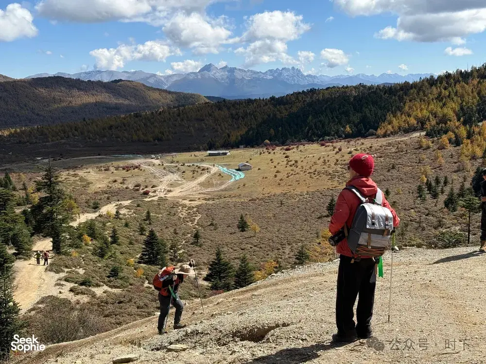 Backpacker looking over a valley from a ridge during the hidden alpine lake trek in Shangri-La, with group hikers below