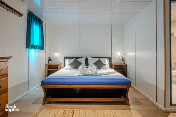 Seaventures Dive Rig cabin bedroom with air-conditioning, a neatly made bed and pillows under soft blue lighting