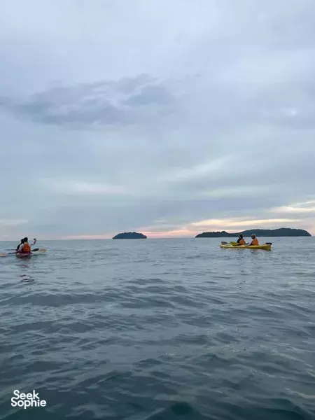 Kayaking in Malaysia in calm open water at dusk, two orange kayaks with paddlers against a cloudy horizon