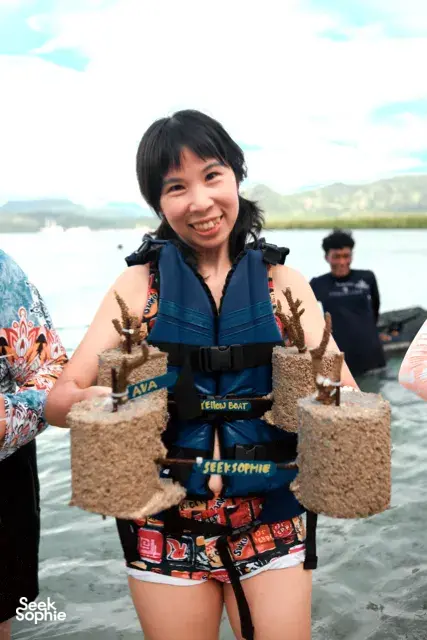 Close-up of a smiling participant holding cement coral plugs in water during coral planting with Rinca Coral Nursery Program in Labuan Bajo