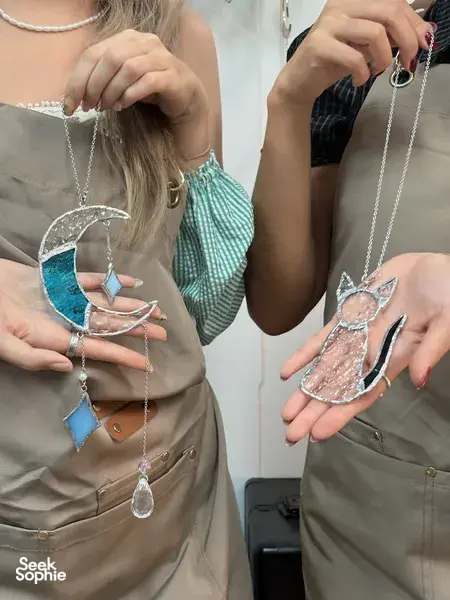 Hands adjusting chains on silver-framed stained-glass suncatcher charms during a Singapore craft session for workshops in Singapore