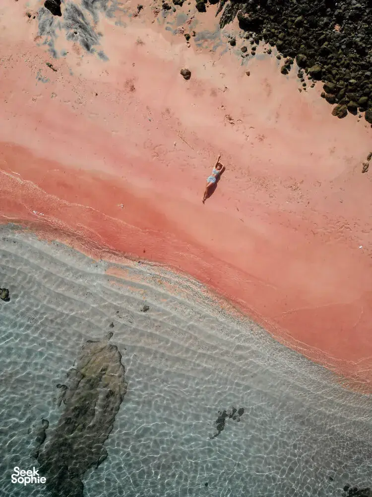 Aerial view of a snorkeller gliding over clear shallow water above pink sand near Komodo Island on the cruise