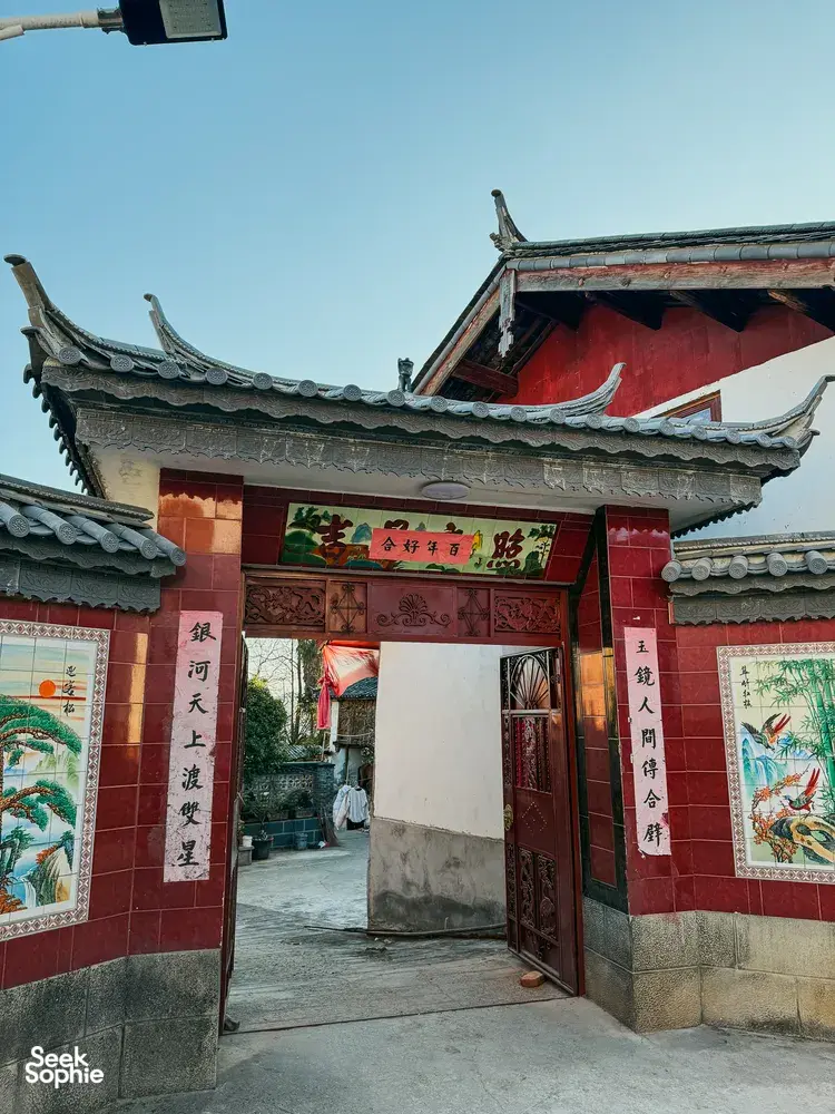 Traditional Naxi-style guesthouse entrance in Lijiang, Yunnan, with red door panels, ornate carvings and tiled roof eaves