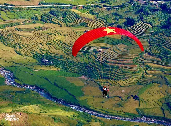 Aerial view of Sapa terraced fields with a red paraglider canopy banking over the valley and river below