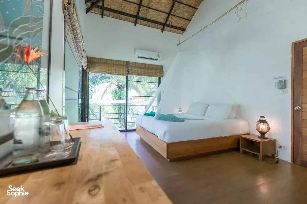 Lounge dining setup beside a mosquito-net bed at Anurak Lodge in Khao Sok National Park, with jungle views from large windows