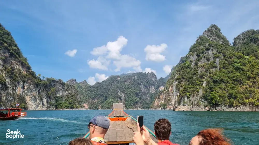 Travellers on a wooden long-tail boat passing limestone cliffs on a private Khao Sok day trip, Cheow Lan Lake
