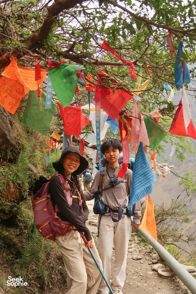 Trekking on the Tiger Leaping Gorge trail in Lijiang with colourful prayer flags overhead as hikers climb a rocky path