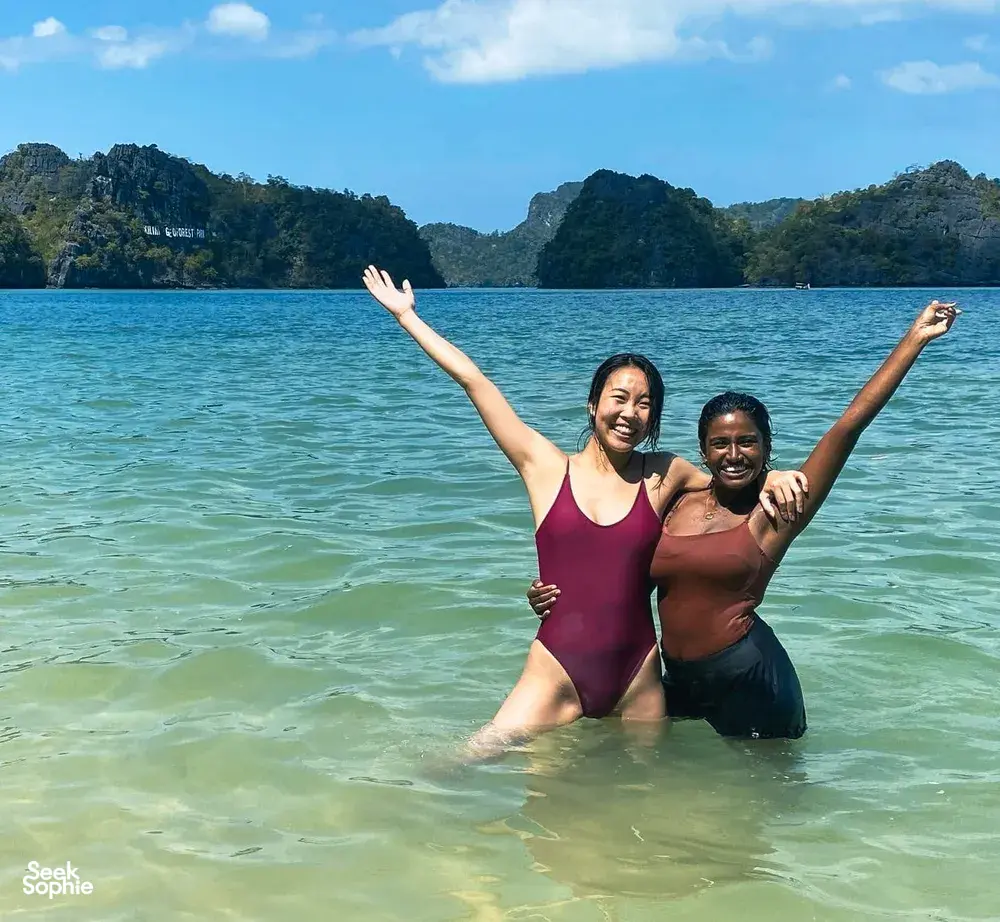 Two paddlers cheering in shallow water off Langkawi, limestone cliffs behind, on a guided Kilim Geoforest kayak outing
