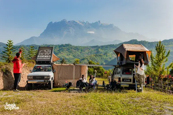 Borneo Overland wild camping base with canvas tents and parked 4x4s, with rolling Sabah valley views, Mt Kinabalu
