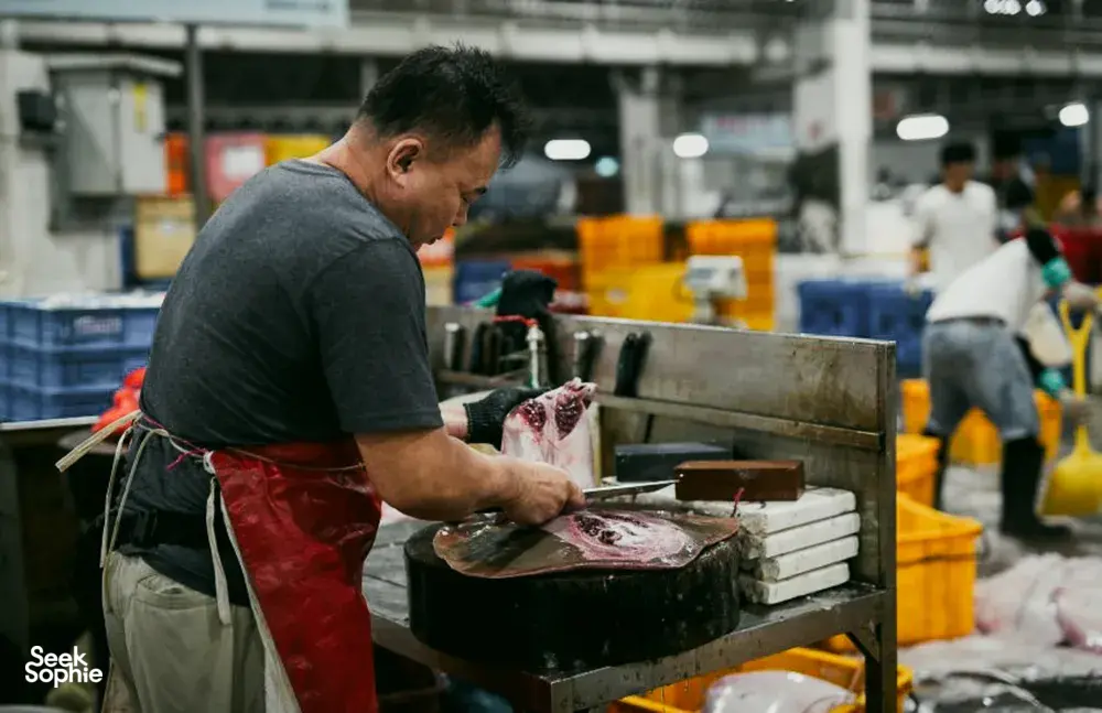 Seorang penjual ikan membersihkan seekor ikan besar di meja kerja logam di pasar ikan Pelabuhan Jurong, Singapura, lalu memotongnya untuk dijual