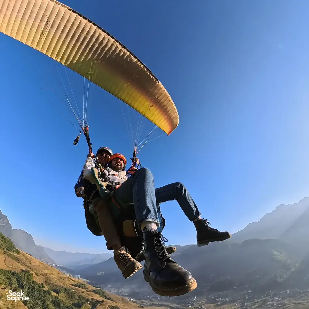 Paragliding tandem riders cradled beneath the amber canopy against the blue sky over mountain valleys, Sapa