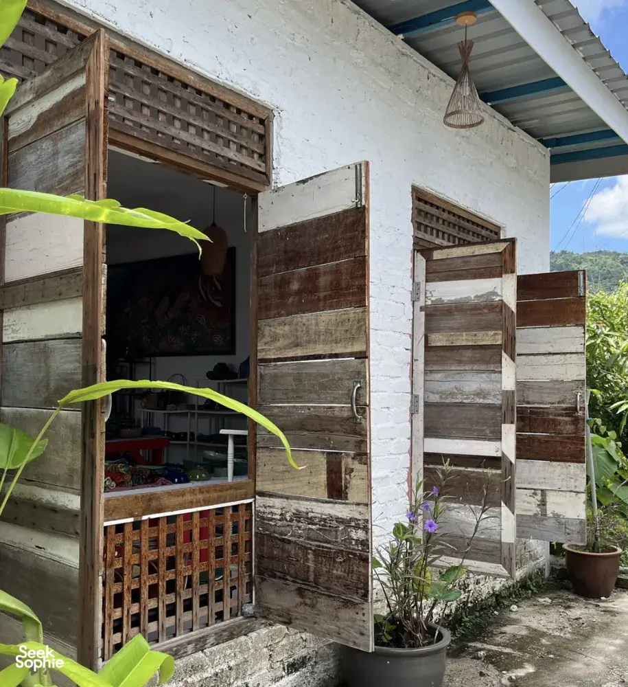 Open wooden studio doors at Ilham Ceramic in Langkawi, revealing a village pottery workspace with tools and tropical greenery.