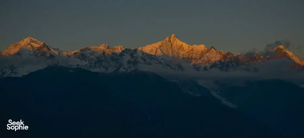 Meili Snow Mountain sunrise view over snow-capped peaks from Shangri-La, with warm light along the ridgeline