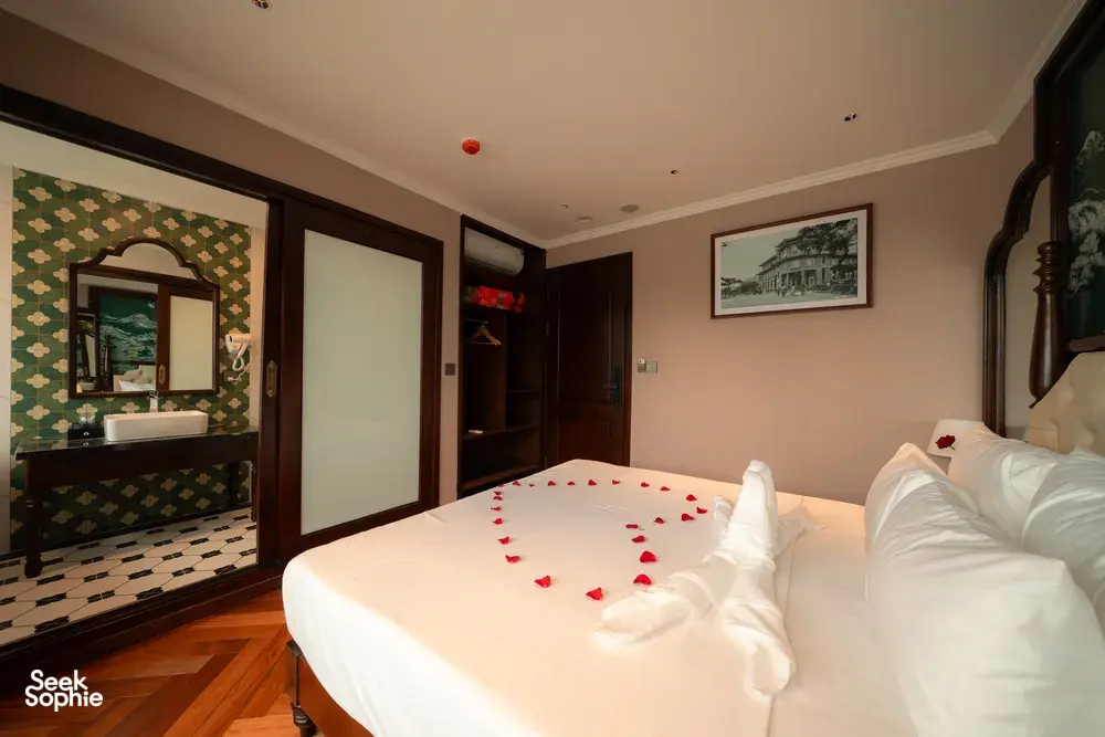 Cruise cabin bedroom with mirror and bathroom doorway, king bed with rose‑petal towel swans, Cat Ba 2D1N