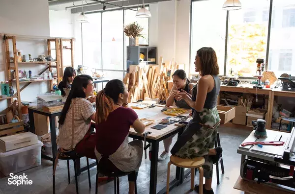 Participants at woodworking jewellery worktables in a bright Singapore studio with tools and shelves around the room — workshops in Singapore