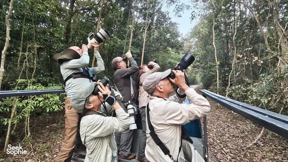 Travellers on an open observation boat scanning the jungle with binoculars during a wildlife-guided tour in Cat Tien, Vietnam
