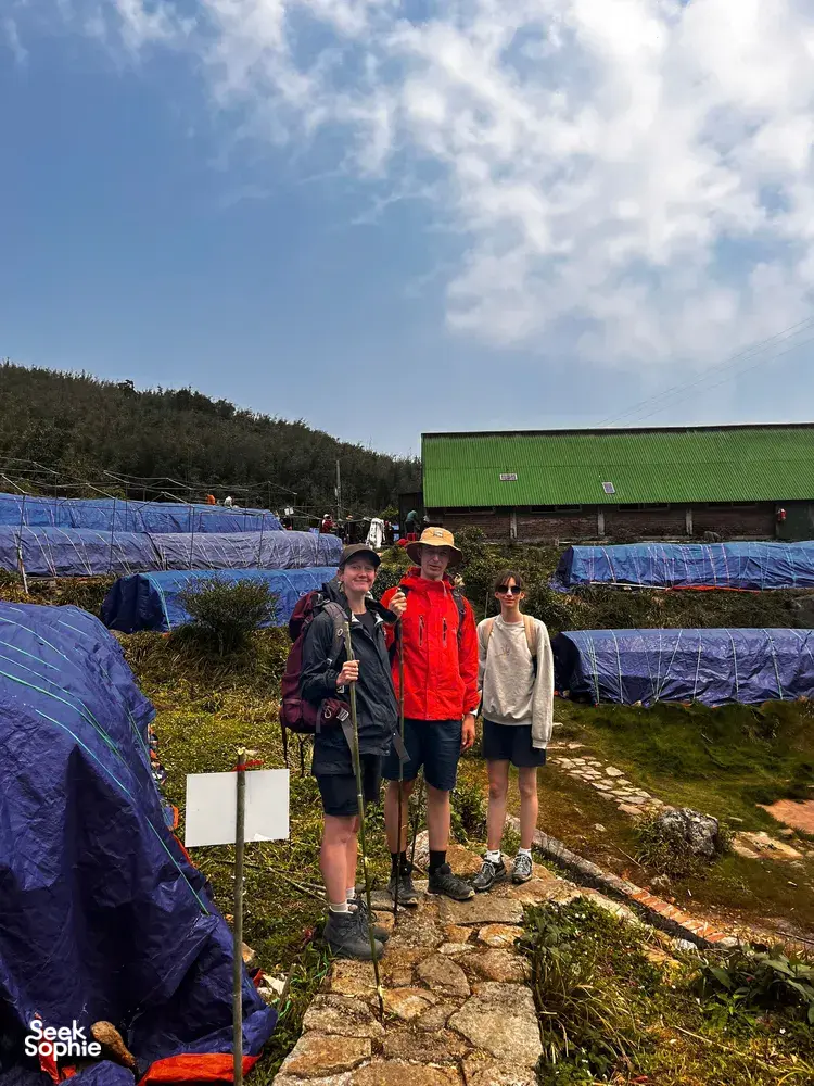 Trekkers standing by blue camping tarps near a green-roof shelter in Sapa during a Fansipan eco trek on the Hmong trail
