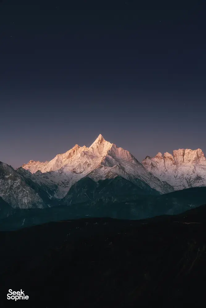 Star-filled night sky over Meili Snow Mountain as dawn light warms the snowy ridges on a 2D2N trek from Shangri-La