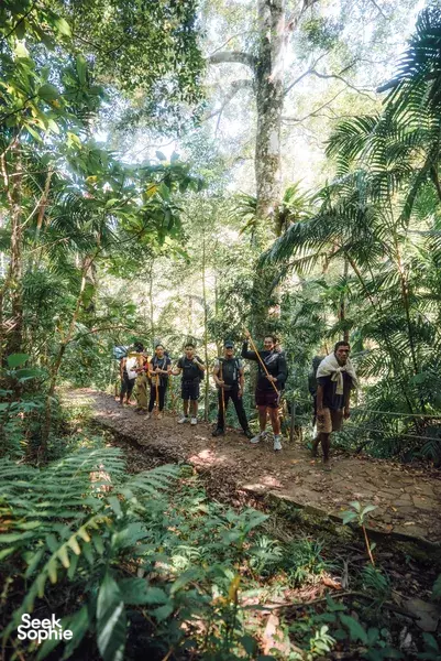 Trekking group walking along a muddy forest path through lush green foliage on an 8D7N Komodo adventure in Labuan Bajo