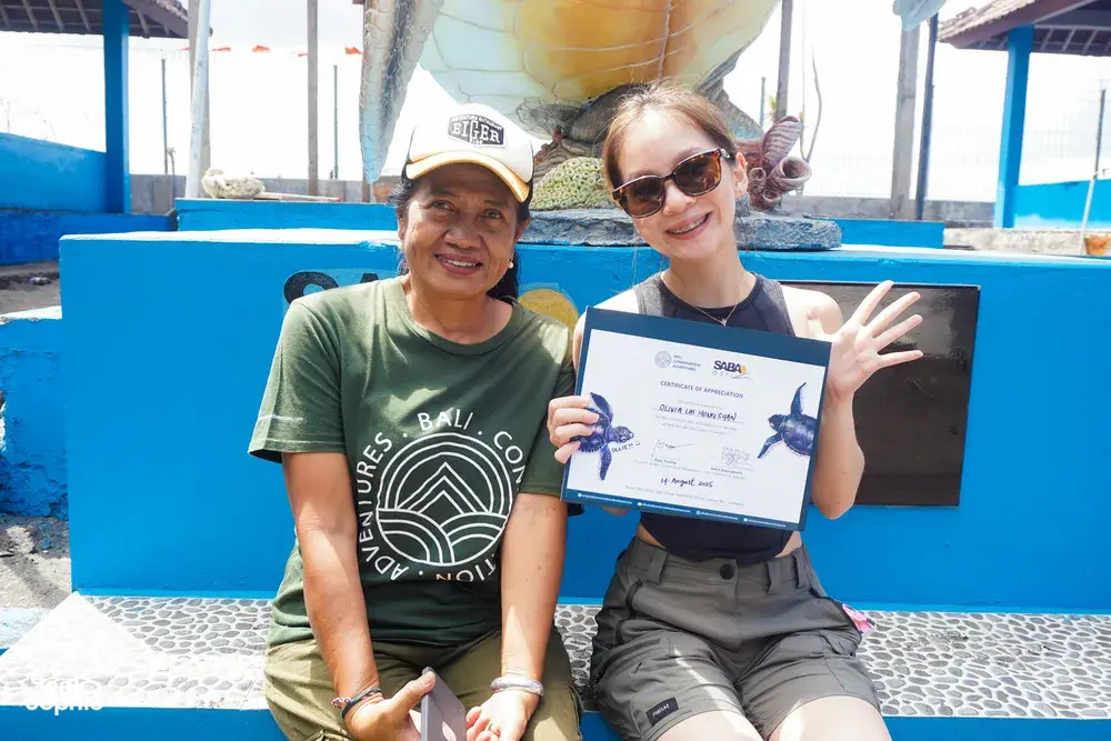 在 Bali Conservation Adventures 的巴厘岛海龟保育中心,两位参与者坐在水池旁,记录下领取证书的时刻