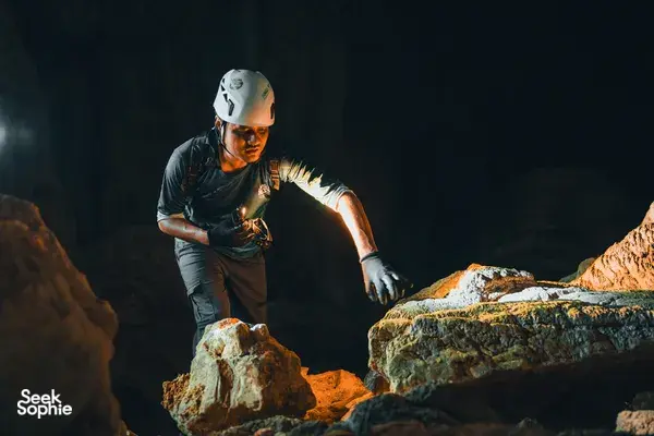 Helmeted trekker standing on boulders inside a dark cave in Phong Nha, set for the cliff-jumping part of the tour