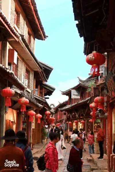 Lantern-lit walkway through Lijiang’s Shuhe Ancient Town, with Naxi-style buildings and people strolling along the lane