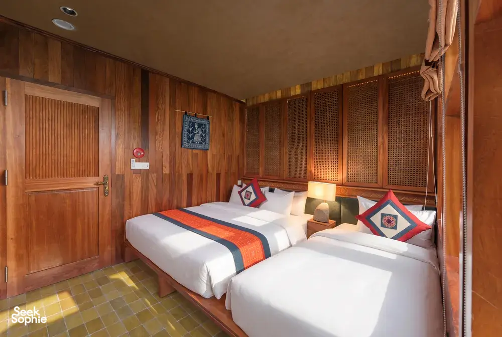 Dual beds in a cosy wooden cabin with stitched cushions and tiled floor, designed for small groups on Cat Ba Ocean Cruises