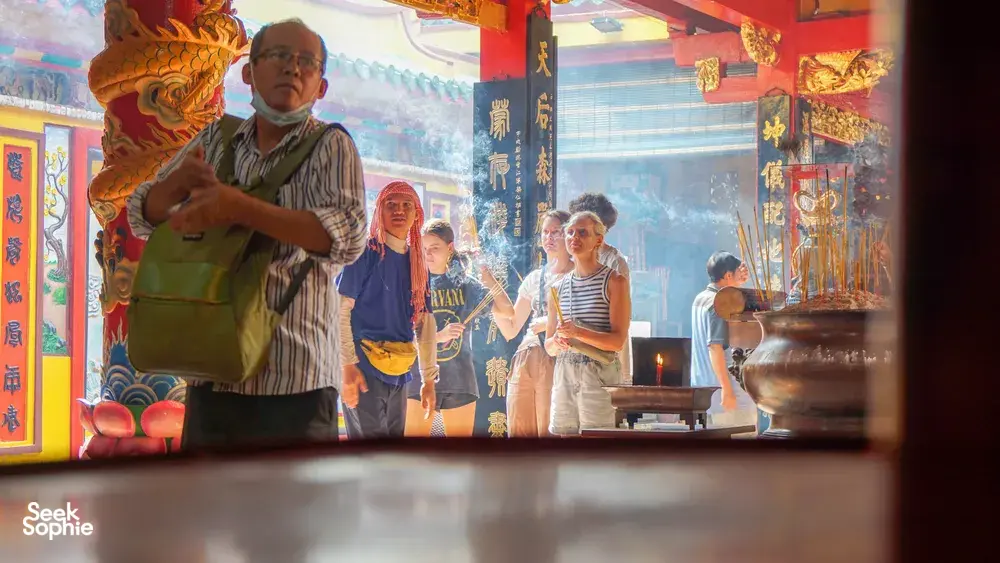 在胡志明市单车之旅中,当地向导在龙壁画与香火缭绕间,向游客指着寺庙祭坛讲解