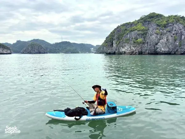 Tien Anh, Cat Ba local fishing enthusiast, paddles a stand-up board on calm bay water near limestone cliffs for hotpot