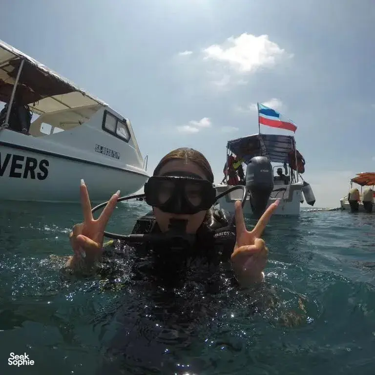 Diver on a boat off Semporna, wearing snorkel mask and wetsuit, flashing peace signs before a reef dive with Bigfin Divers