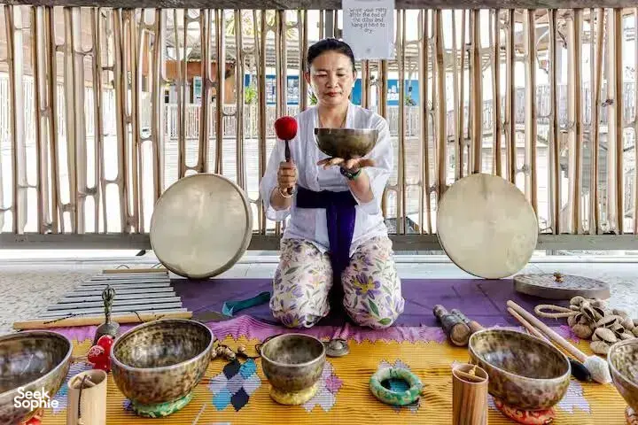 ADDA Yoga practitioner holding a sound-healing mallet with singing bowls on a rooftop mat in Bali, Canggu