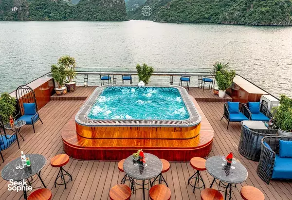 La Casta cruise sundeck hot tub and round lounge tables, framed by palm planters and calm water in Halong Bay