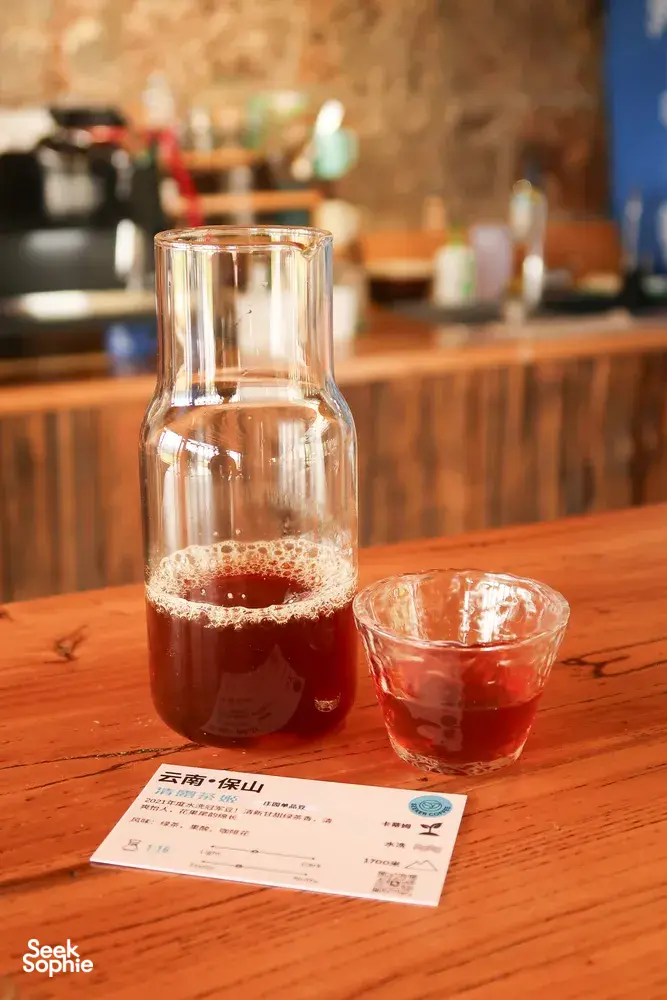 Glass carafe of Yunnan coffee and a tasting cup on a wooden table during a Seeker Yunnan Coffee Estate cupping session in Lijiang