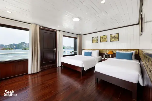 Twin cabin with two beds, blue headboard cushions and large windows showing Halong Bay limestone scenery outside