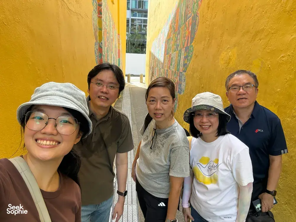 Group posing by a yellow mural wall in Katong-Joo Chiat during the real-life Monopoly experience, Singapore for team building Singapore