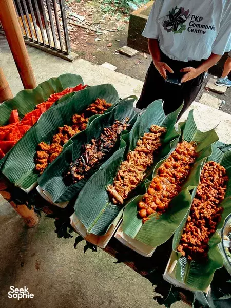 Rows of grilled skewers arranged on banana leaves at a community event in Indonesia, with a person standing nearby