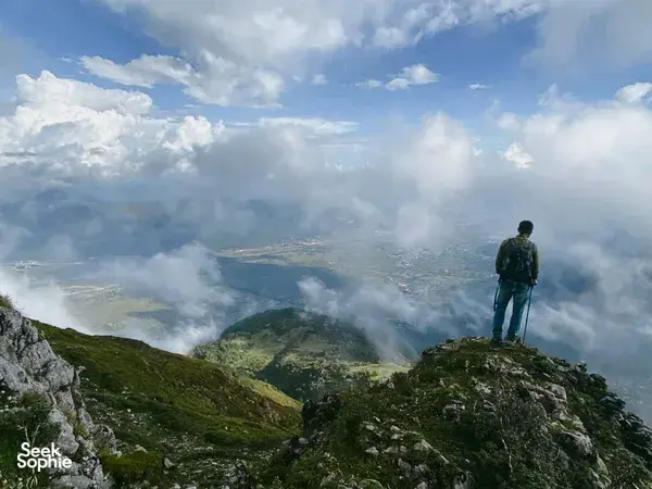Hiker with trekking poles standing on a rocky ridge as mist and clouds drift over valleys during the Jade Dragon hike